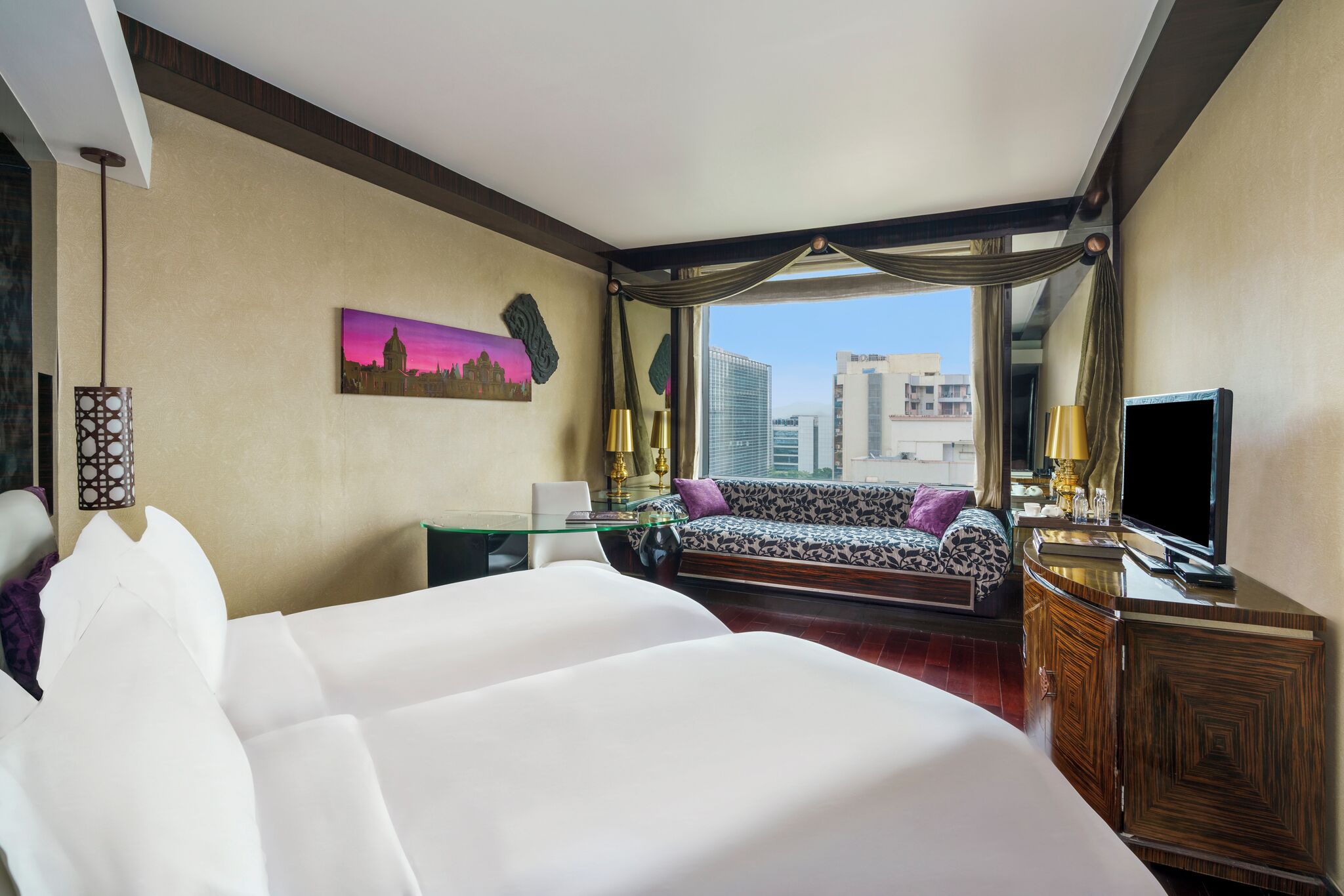 A hotel room with a large bed, a sofa, a TV, and a view of the cityscape.