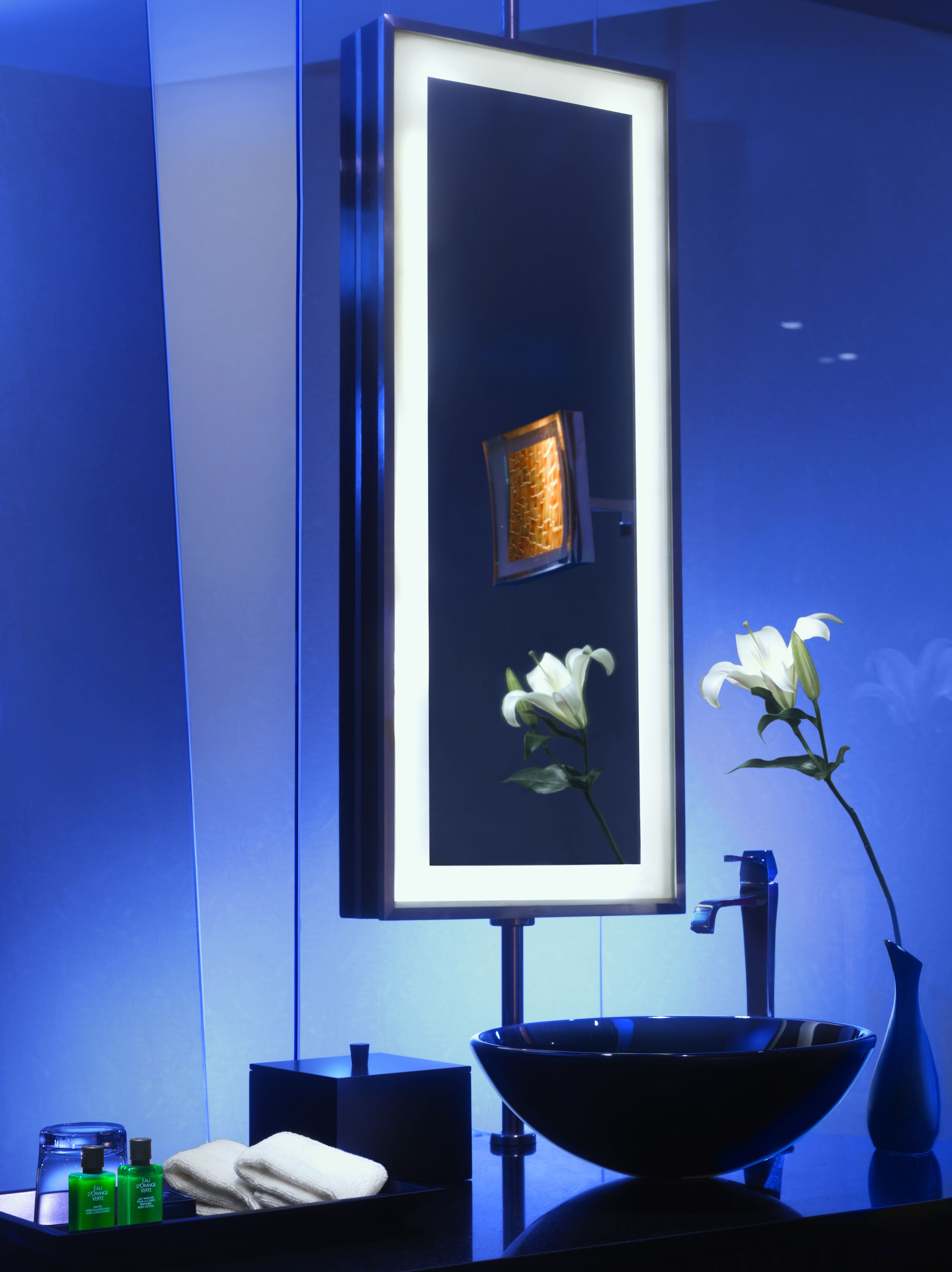 A modern bathroom with a large mirror, a black sink, and a vase with a white flower.