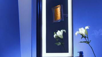 Een moderne badkamer met een grote spiegel, een zwarte wastafel en een vaas met een witte bloem.