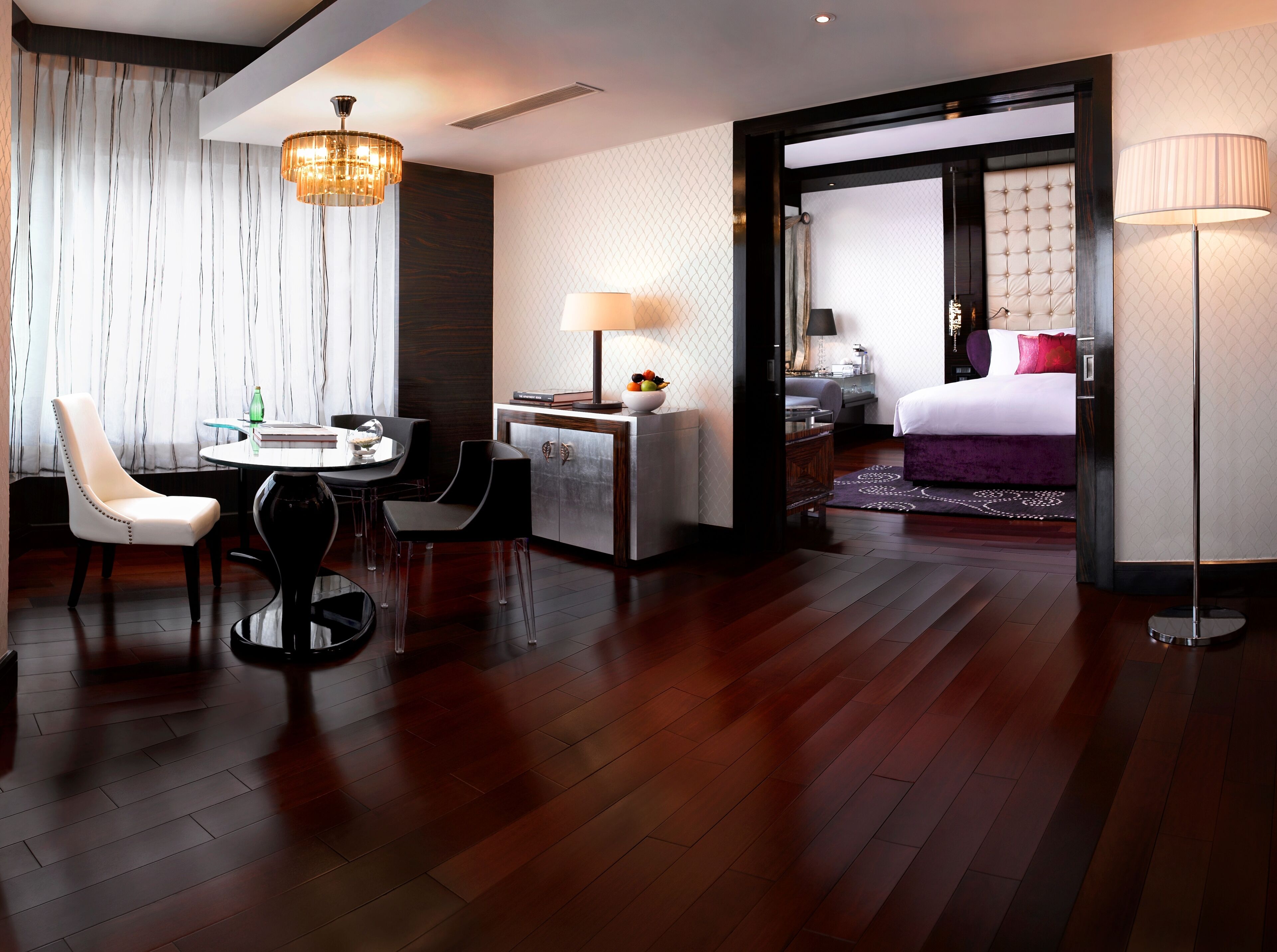 A hotel room with a dining area, a bed with a tufted headboard, and a large window with curtains.