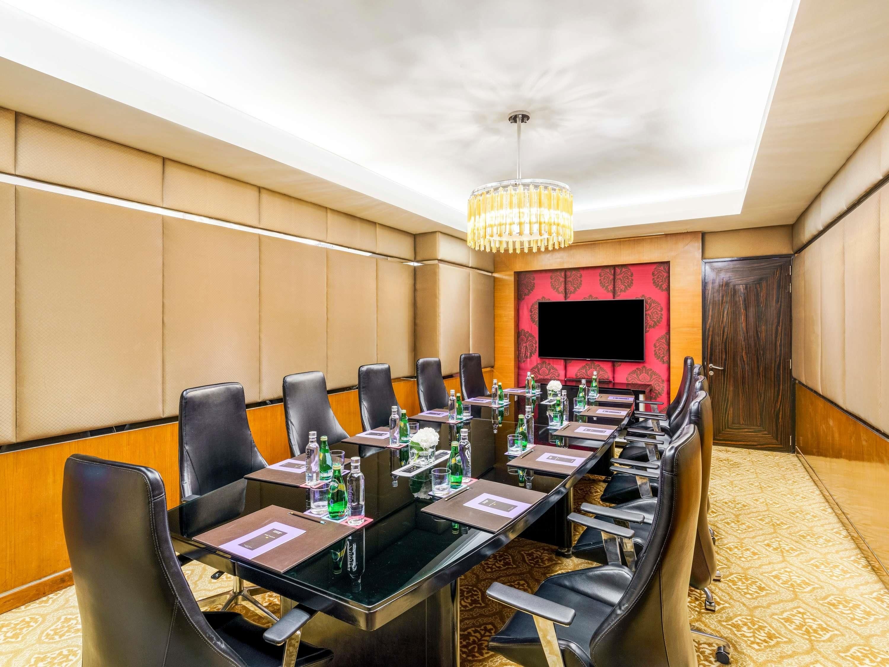 A conference room with a long table, chairs, a chandelier, a TV, and a patterned carpet.