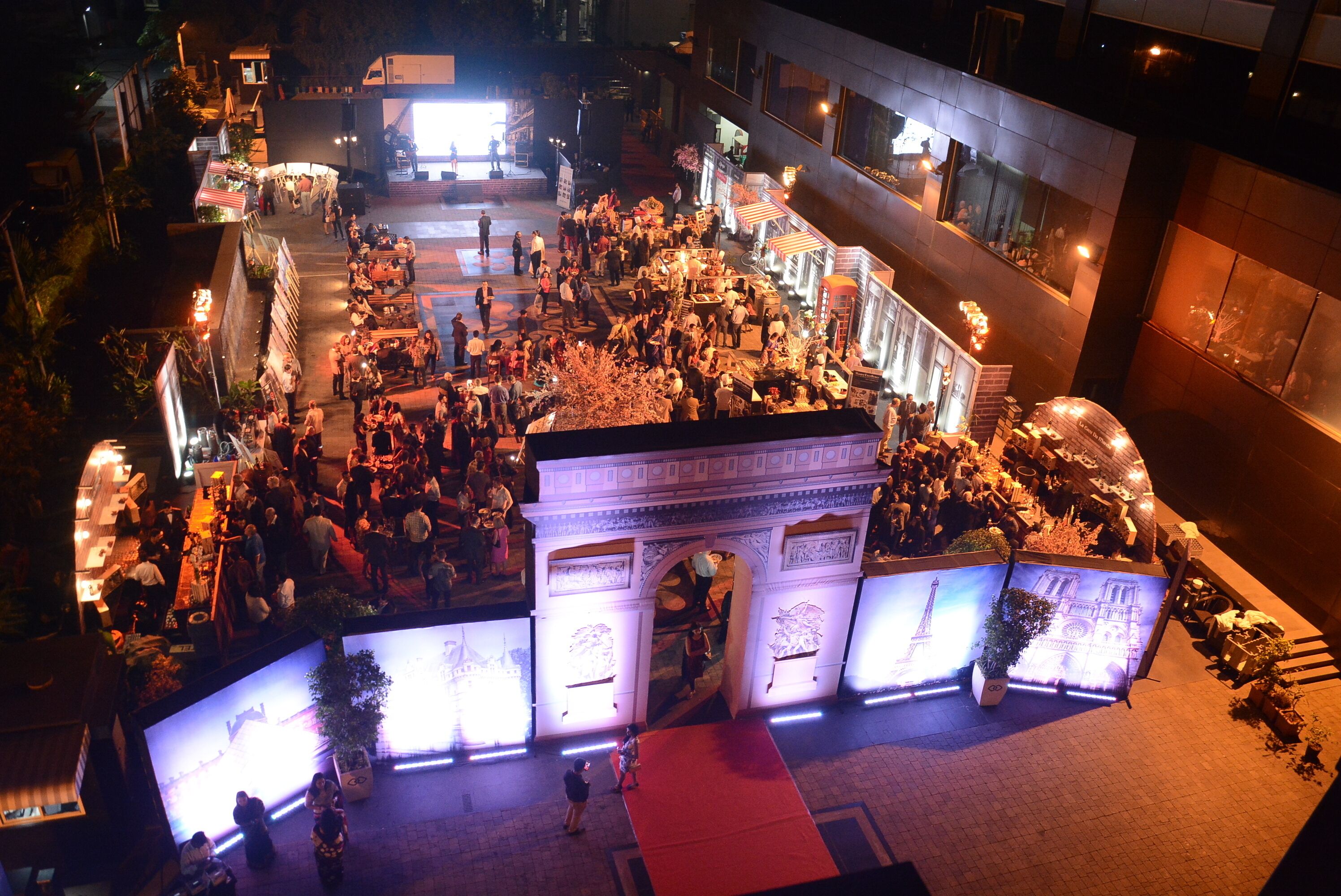 A crowded outdoor event with illuminated arches and a central stage.