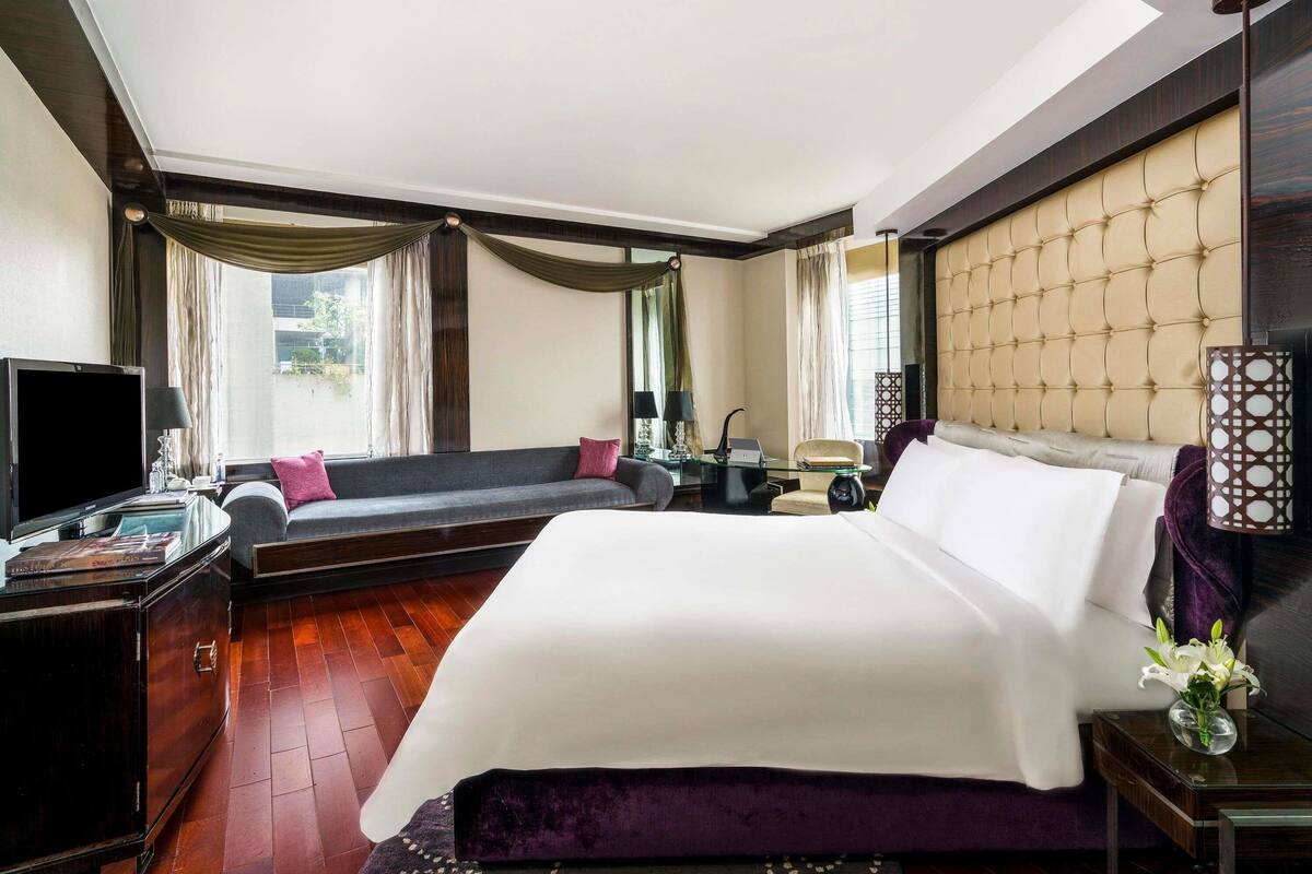 A hotel room with a bed, a sofa, a TV, a desk, and a window with curtains.