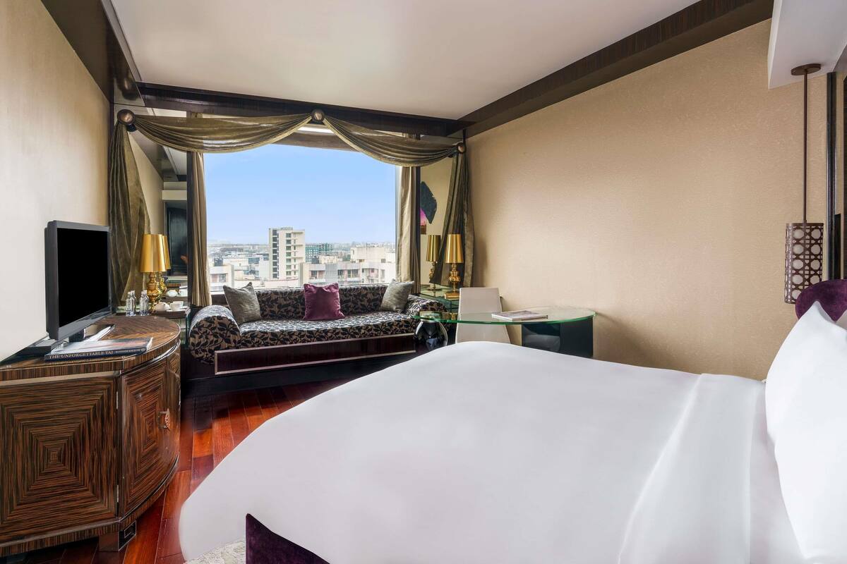 A hotel room with a bed, a sofa, a TV, a desk, and a view of the city.