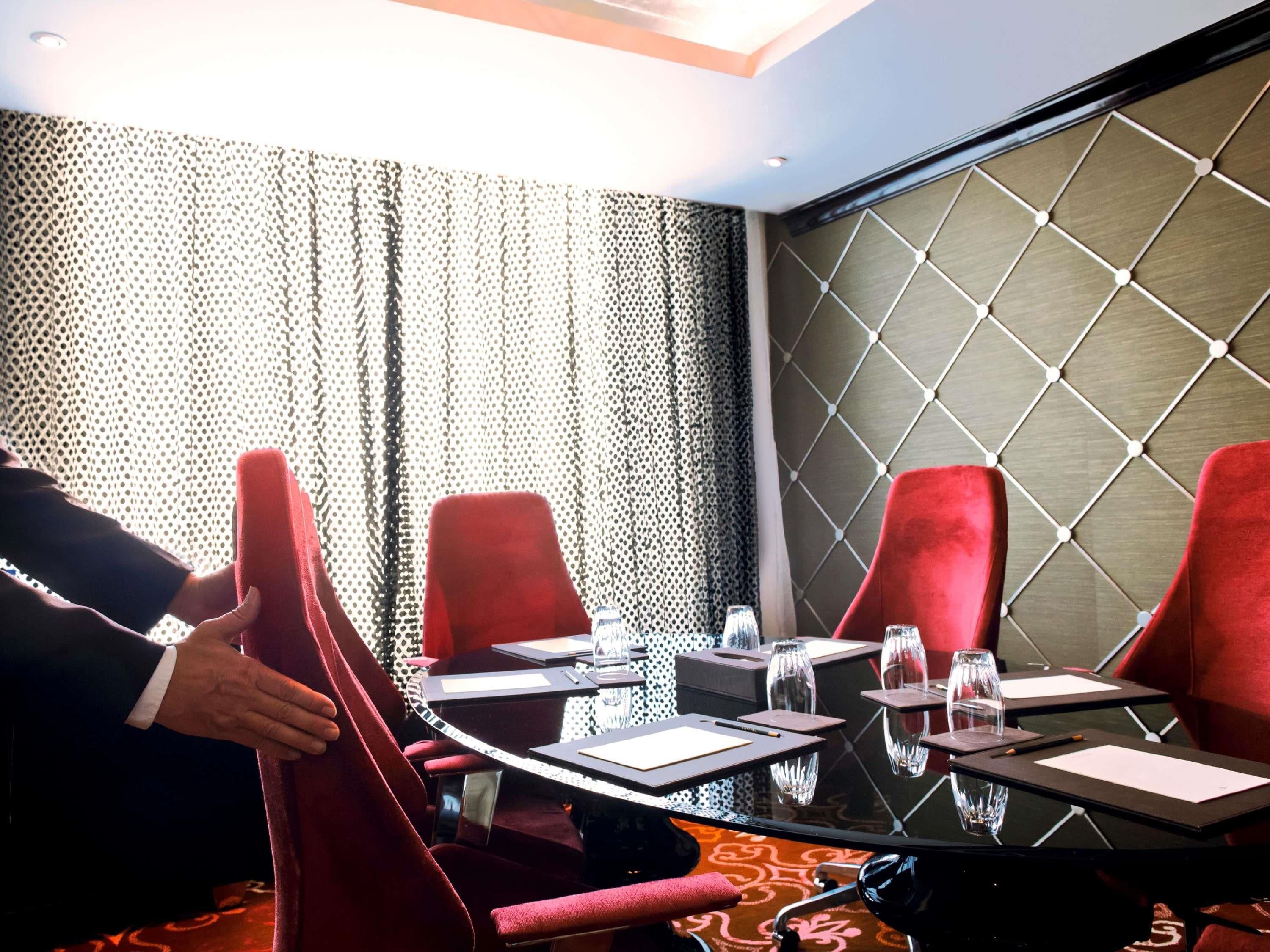 A conference room with a glass table, red chairs, and a patterned wall.