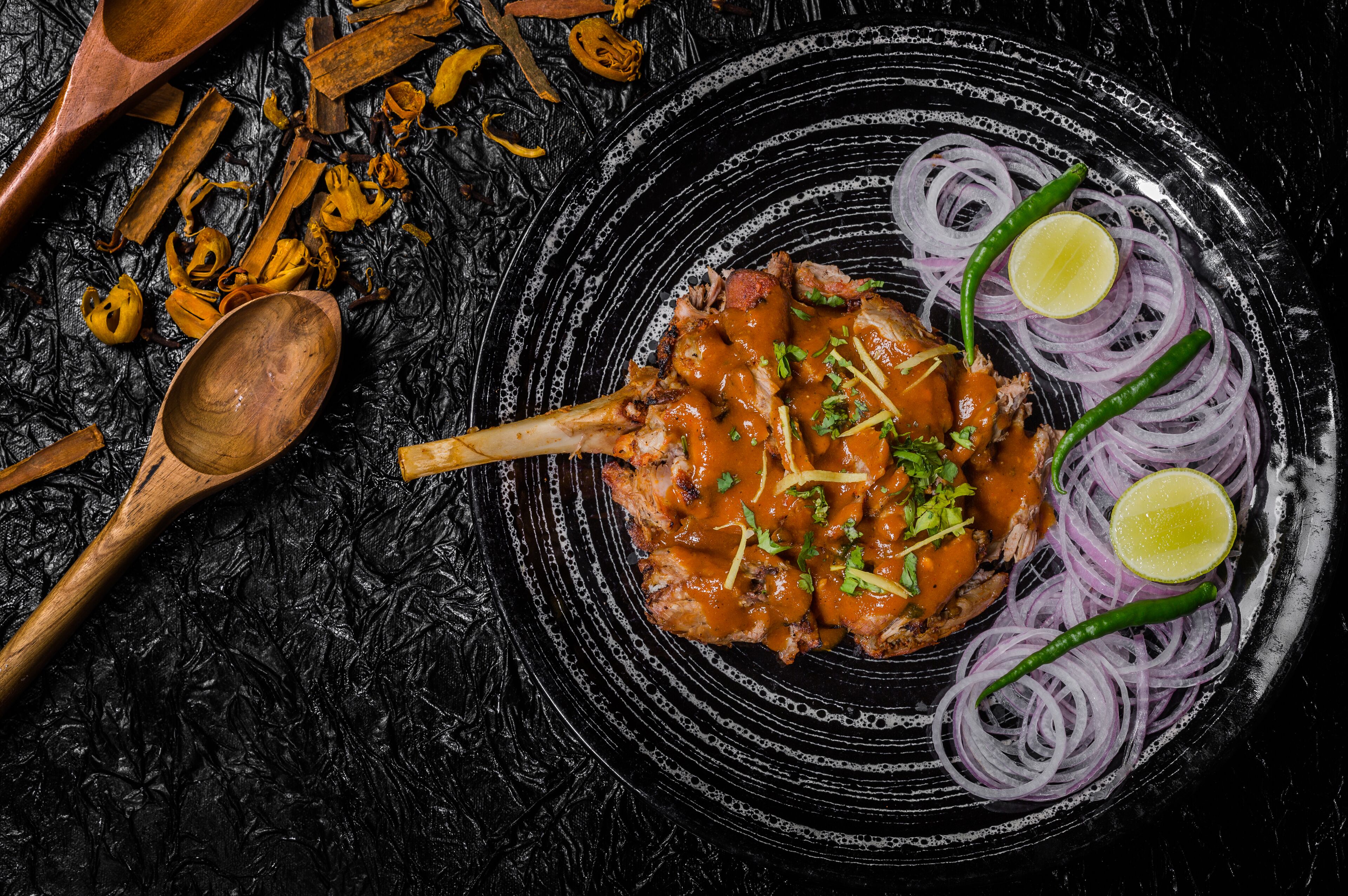 Une assiette de nourriture comprenant un plat de viande, des oignons et des tranches de citron vert, le tout posé sur une surface noire texturée.