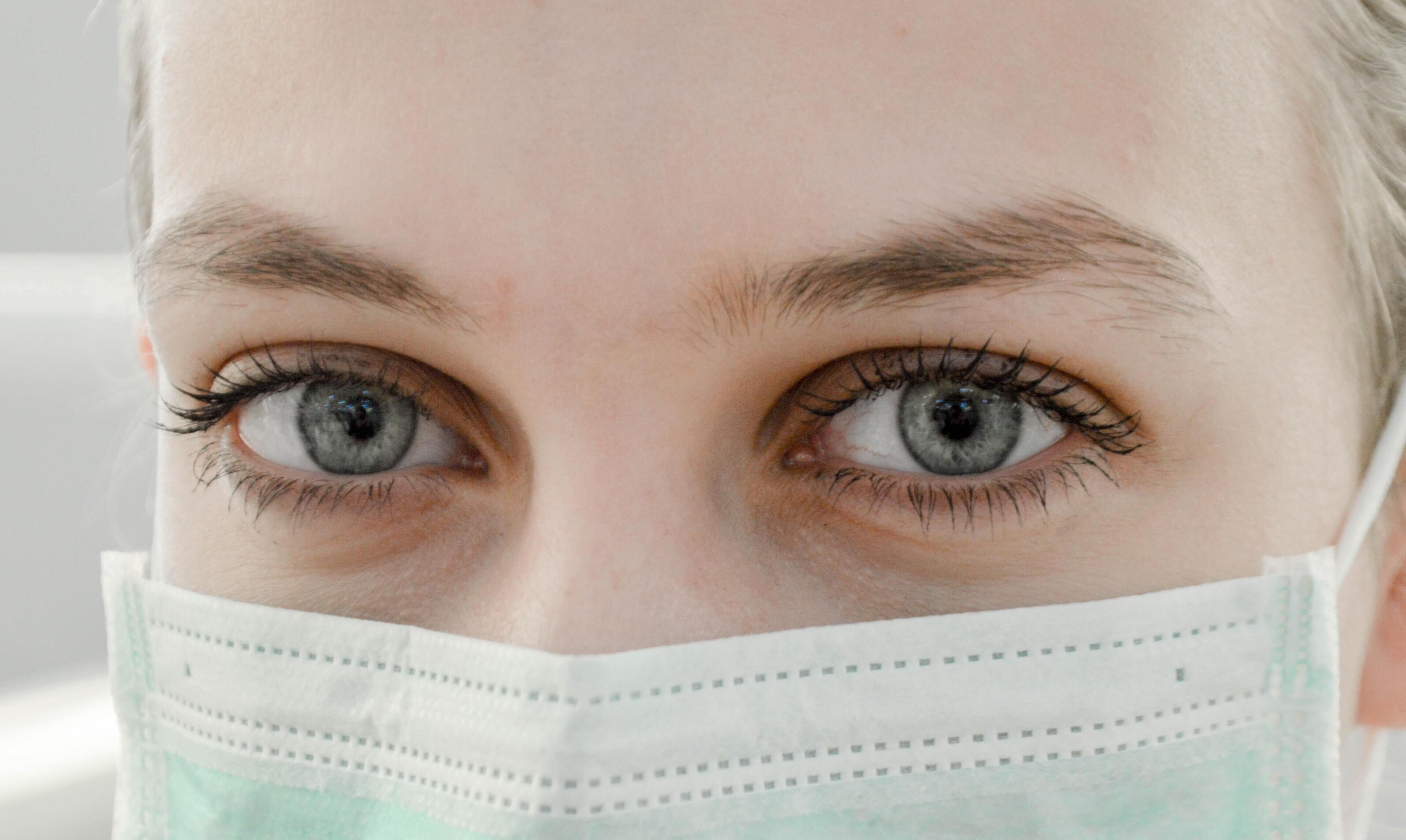 A close-up of a person's face with visible eyes and a surgical mask.