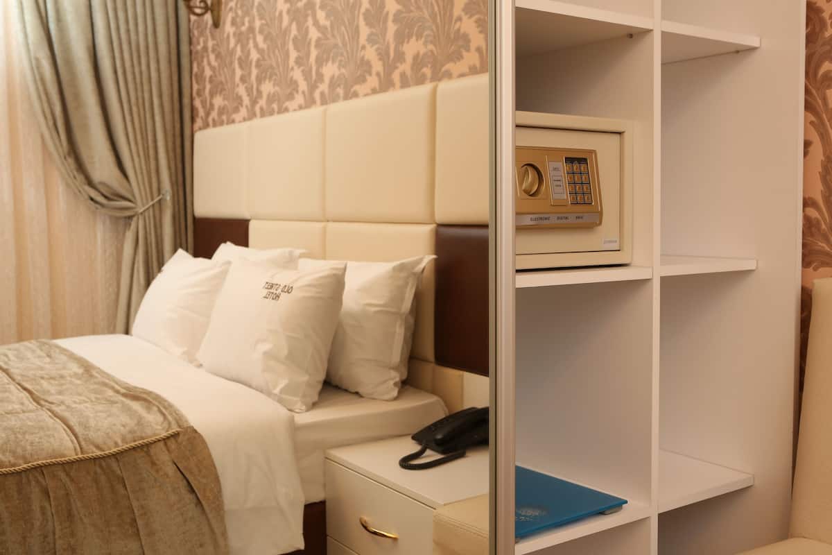 Een hotelkamer met een bed, een nachtkastje met een telefoon, een plank met een boek en een aan de muur bevestigd elektronisch apparaat.