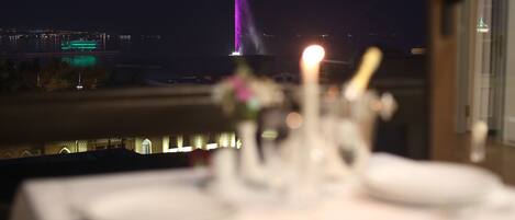 Mesa para dos, servida con una vela, con vistas a un paisaje urbano nocturno.