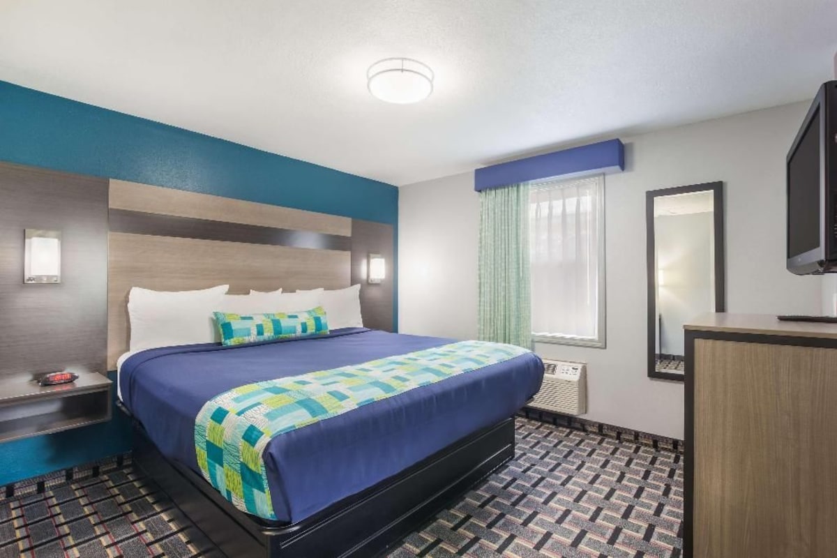 A hotel room with a bed, bedside table, TV, and a window with curtains.