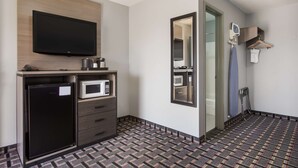 Une chambre d’hôtel équipée d’un téléviseur à écran plat, d’un mini-réfrigérateur, d’un four à micro-ondes, d’un petit meuble, d’un miroir et d’un sol à motifs.
