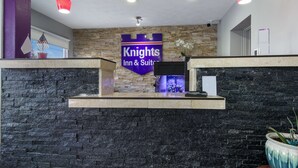 Un comptoir d’accueil avec un mur en pierre en arrière-plan, une enseigne indiquant « Knights Inn & Suites » et une plante en pot.