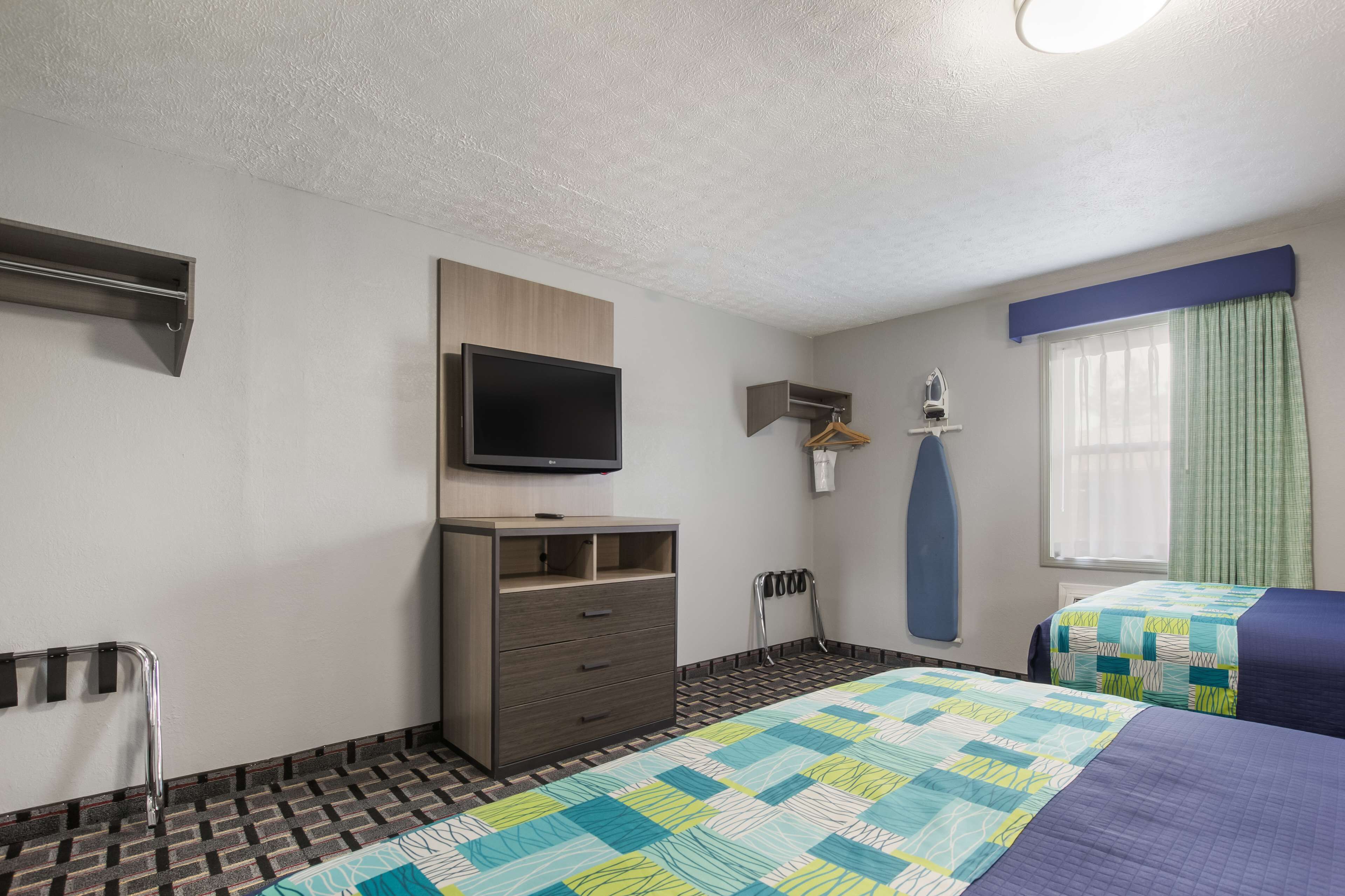 Une chambre d’hôtel comprenant un lit, une télévision, une commode, une fenêtre avec des rideaux et un espace douche.
