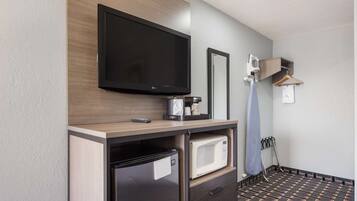 A compact hotel room with a flat-screen TV, a mini-fridge, a microwave, a small coffee maker, a mirror, and a clothing rack.