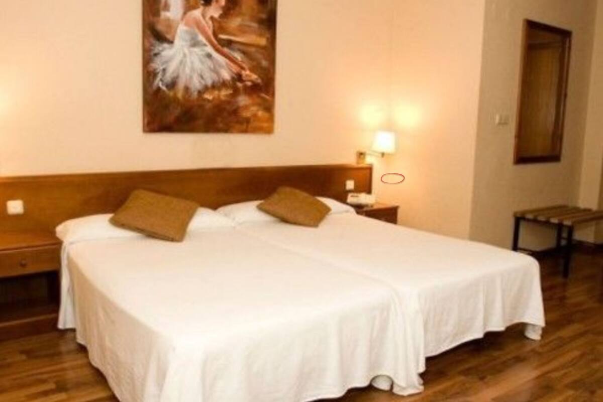 Ein Doppelbett mit weißen Leinen und zwei Kissen, ein hölzernes Kopfteil, ein Nachttisch mit Lampe sowie ein Bild an der Wand.