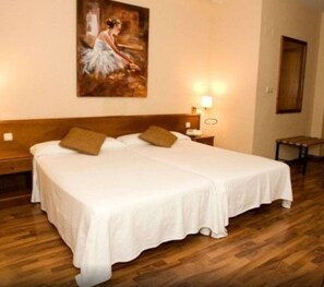 Una cama doble con sábanas blancas y dos almohadas, un cabecero de madera, una mesita de noche con lámpara y un cuadro en la pared.