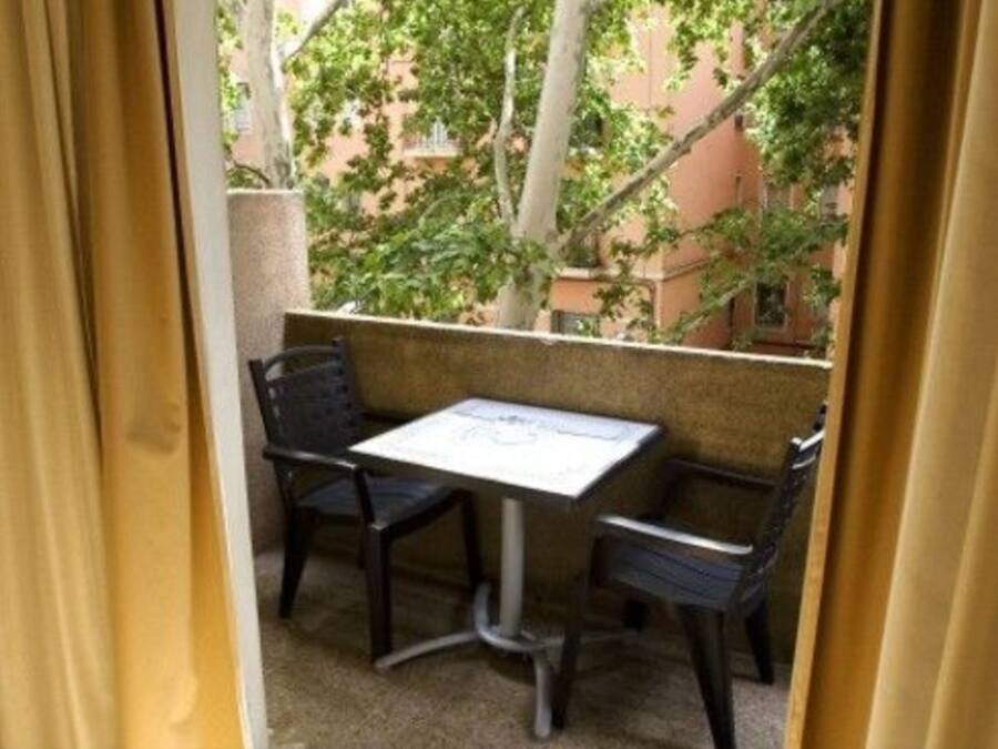 A small outdoor seating area with a table and two chairs, surrounded by a low wall and greenery.