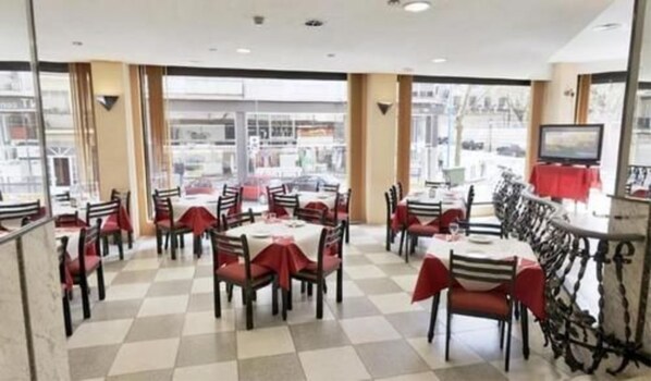 Um restaurante com chão quadriculado, cadeiras vermelhas e mesas.