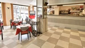 Un restaurante con piso a cuadros, mesas con manteles rojos y una zona de bar con botellas.