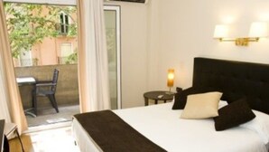 Habitación de hotel con cama, mesita de noche, lámpara, silla y vistas al exterior.
