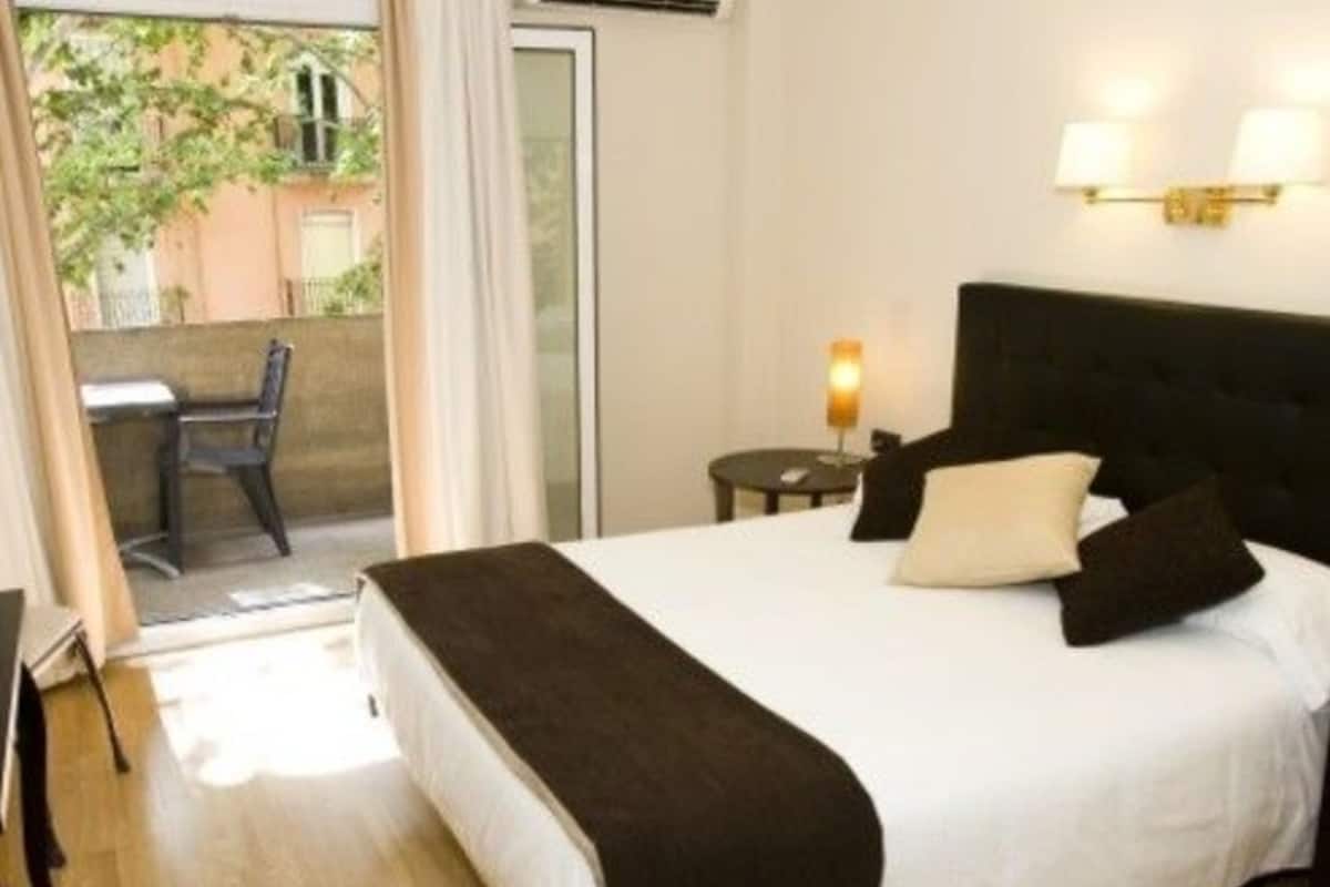 Ein Hotelzimmer mit Bett, Nachttisch, Lampe, Stuhl und Blick nach draußen.