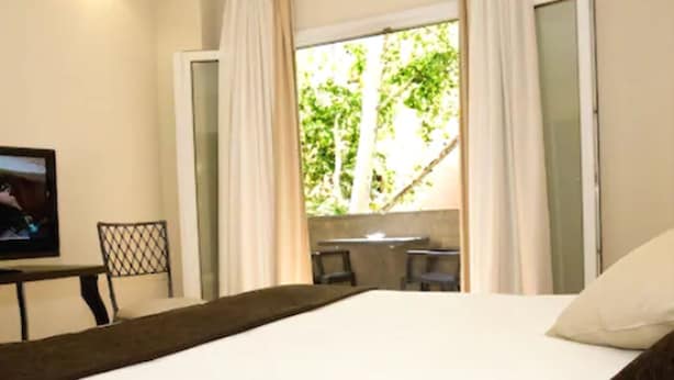 Un dormitorio con cama, televisor, escritorio y ventana con cortinas.
