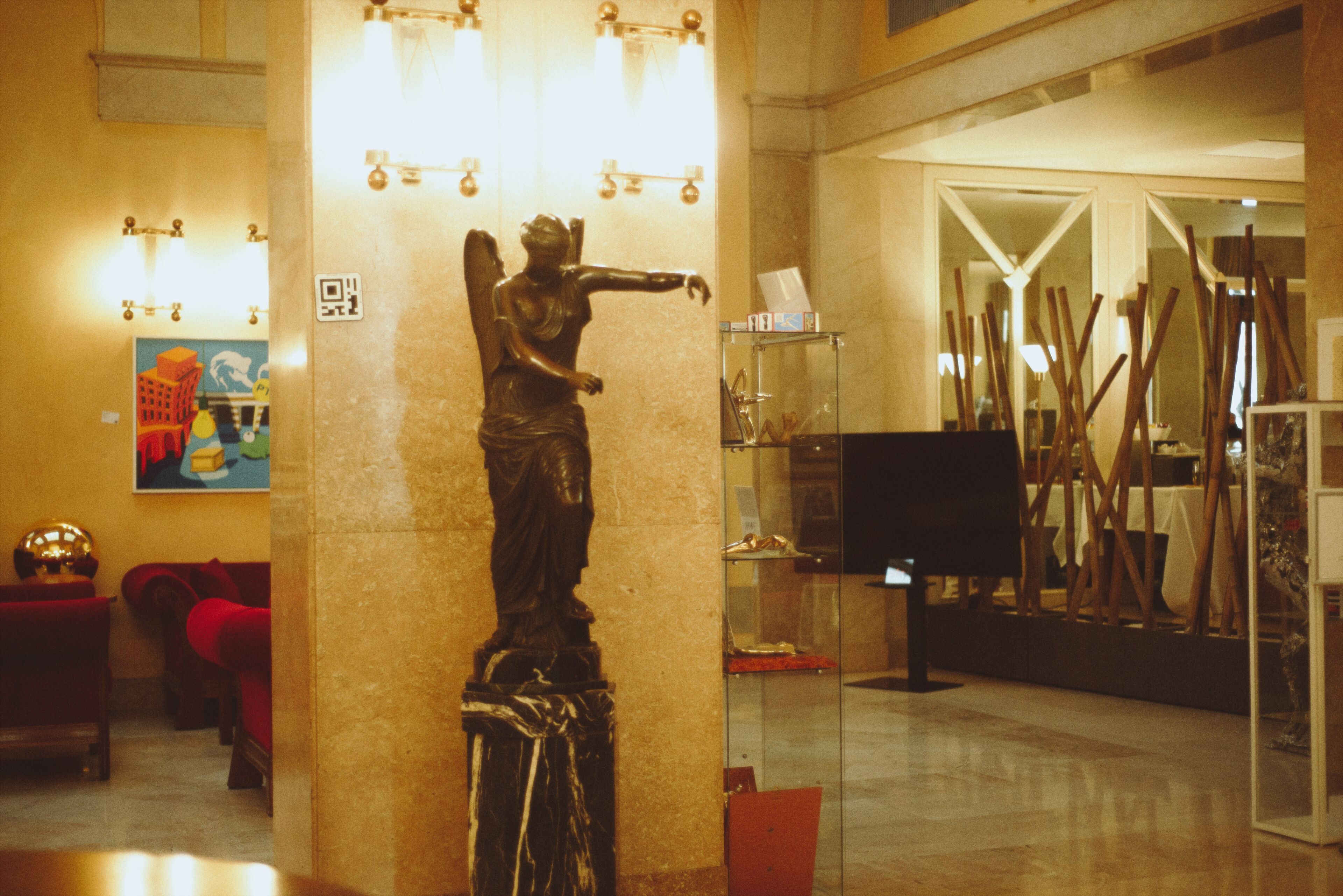 A statue in a lobby with a glass display case and a painting on the wall.