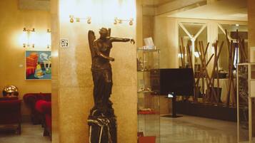 A statue in a lobby with a glass display case and a painting on the wall.