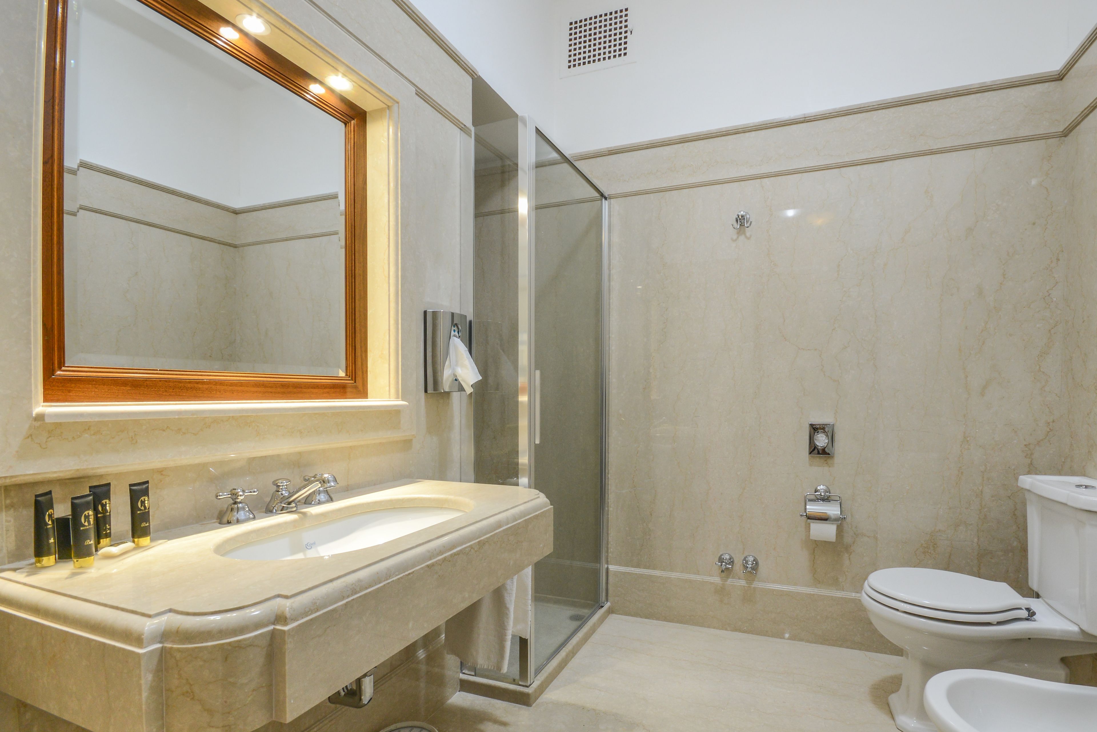 A modern bathroom with a large mirror, a double sink vanity, a glass-enclosed shower, and a toilet.