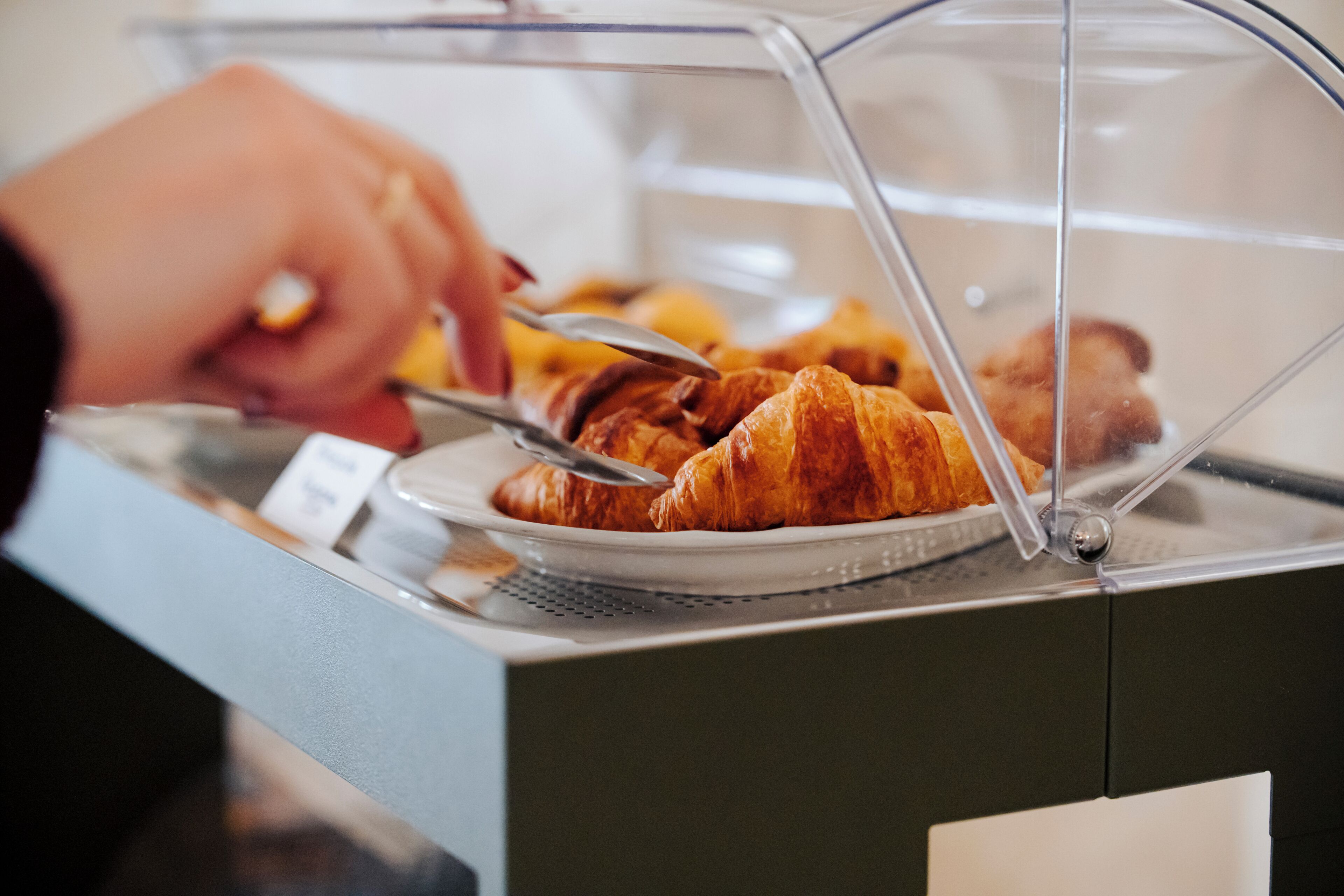 A hand reaching for a croissant from a glass display case.