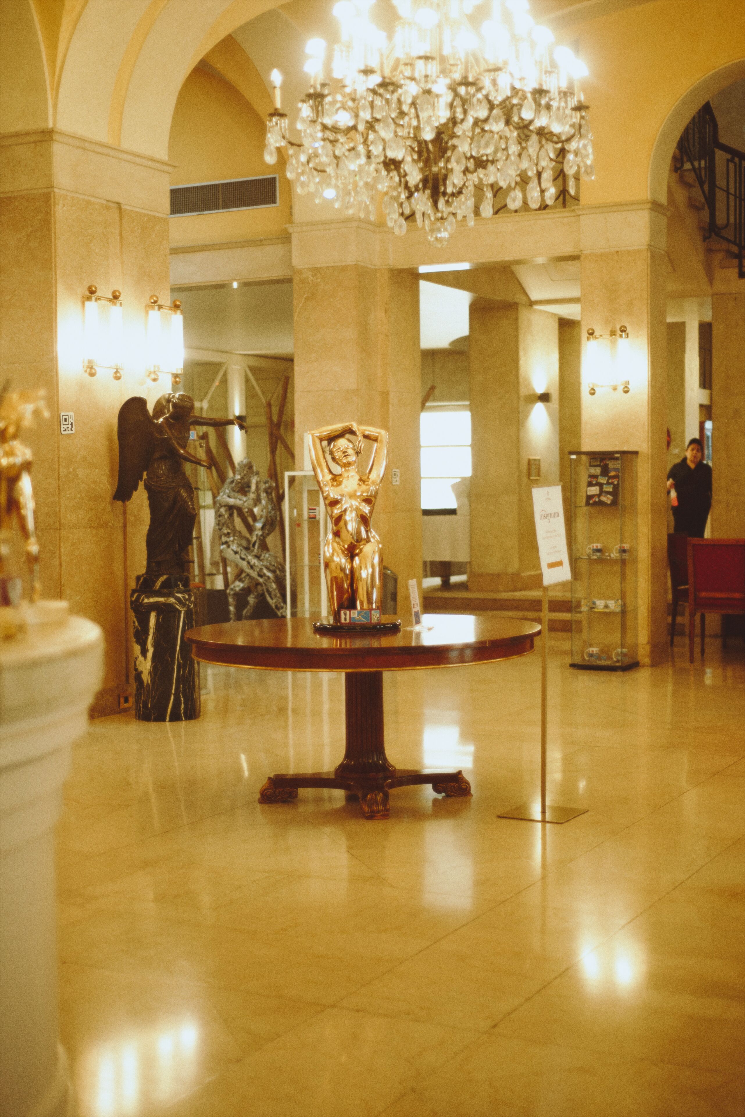 A lobby with a chandelier, statues, and a reception desk.