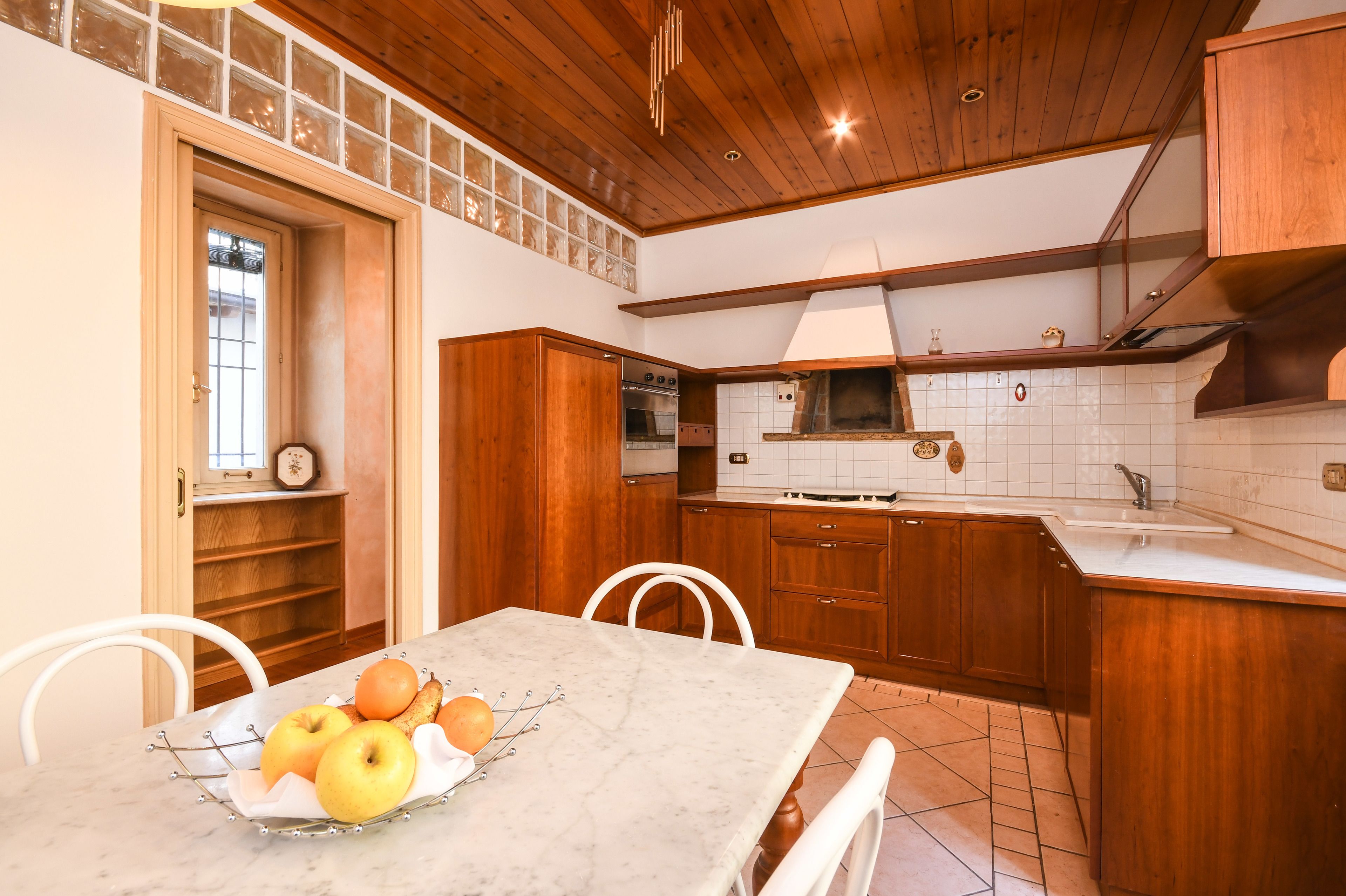 Une cuisine avec des meubles en bois, un plan de travail en marbre et une table à manger agrémentée d’un panier de fruits.