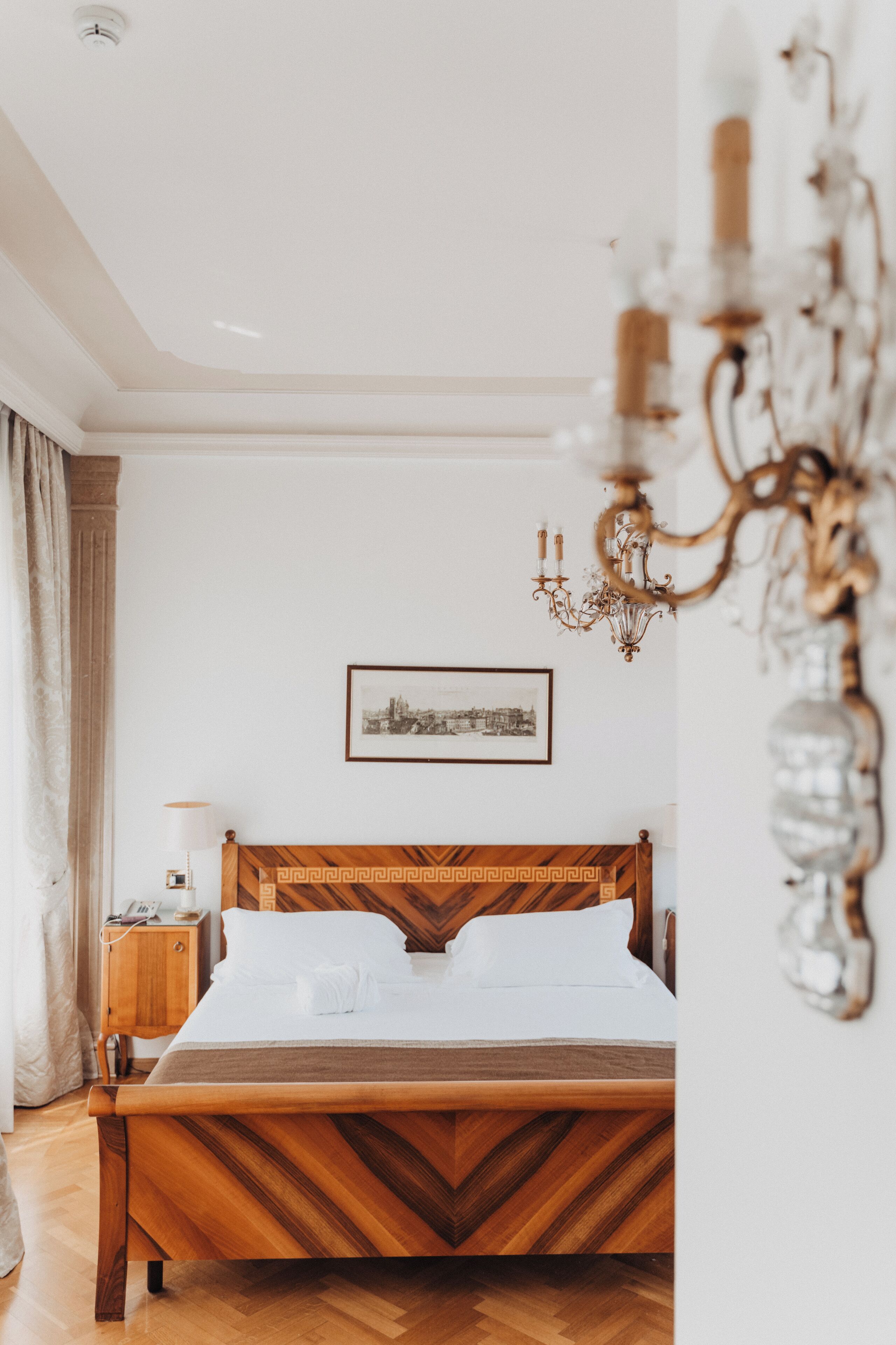 Una camera da letto con un letto di legno, un comodino, una lampada, un lampadario e un quadro appeso al muro.