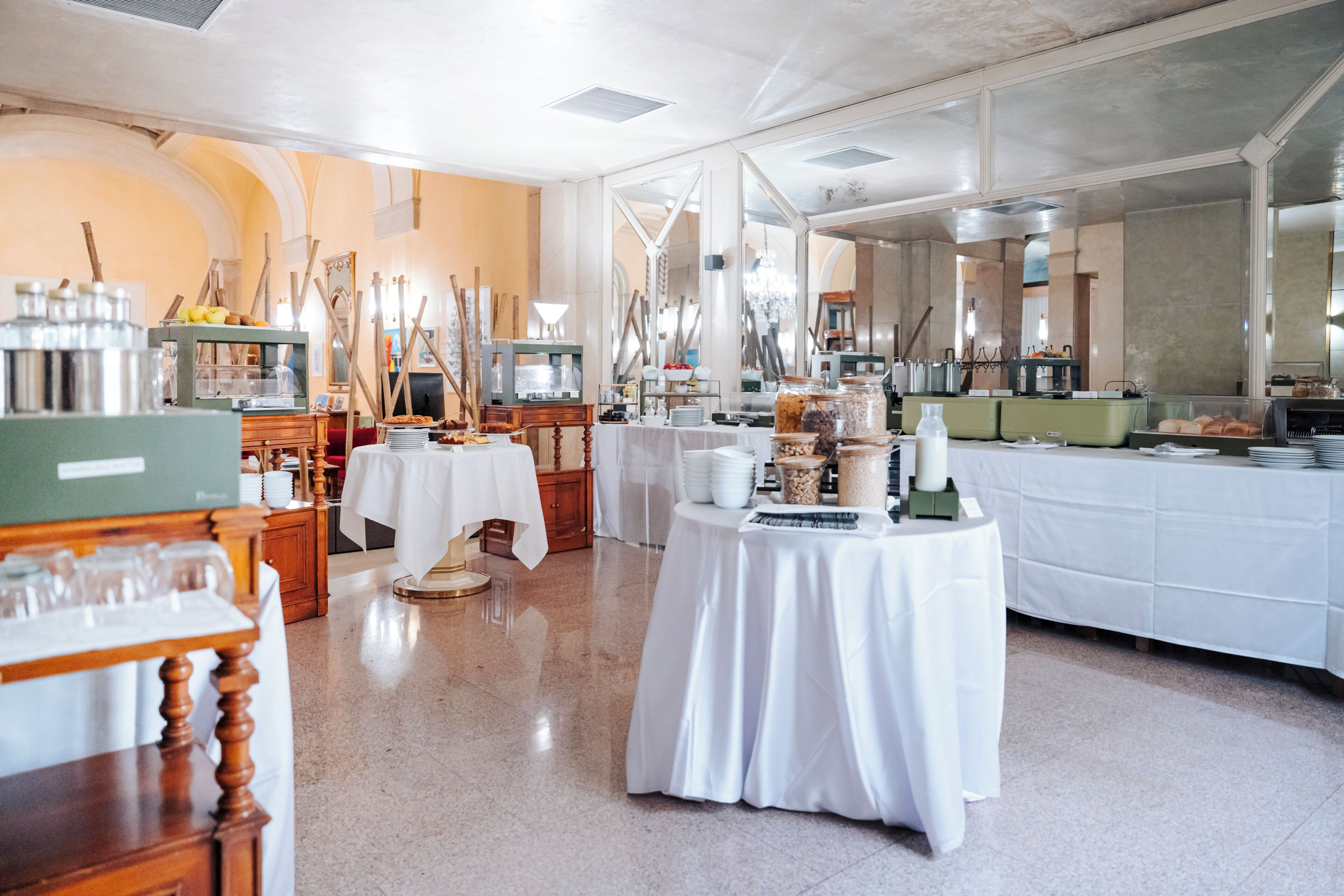 Un amplio comedor con mesas dispuestas para el servicio, una barra de buffet y un espejo grande que refleja la sala.