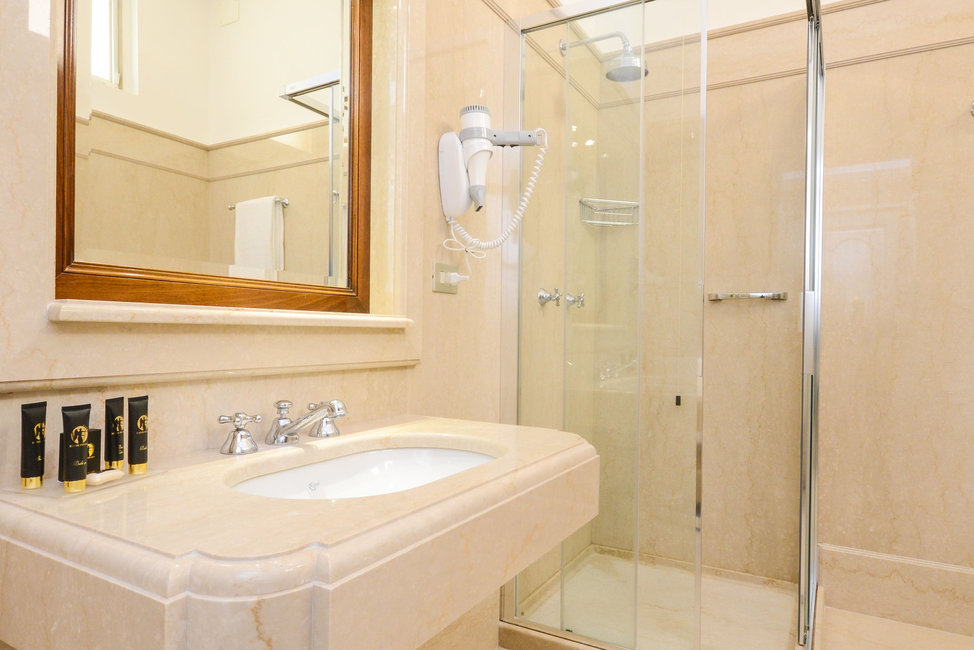 A bathroom with a marble sink, a large mirror, a hairdryer, and a glass-enclosed shower.