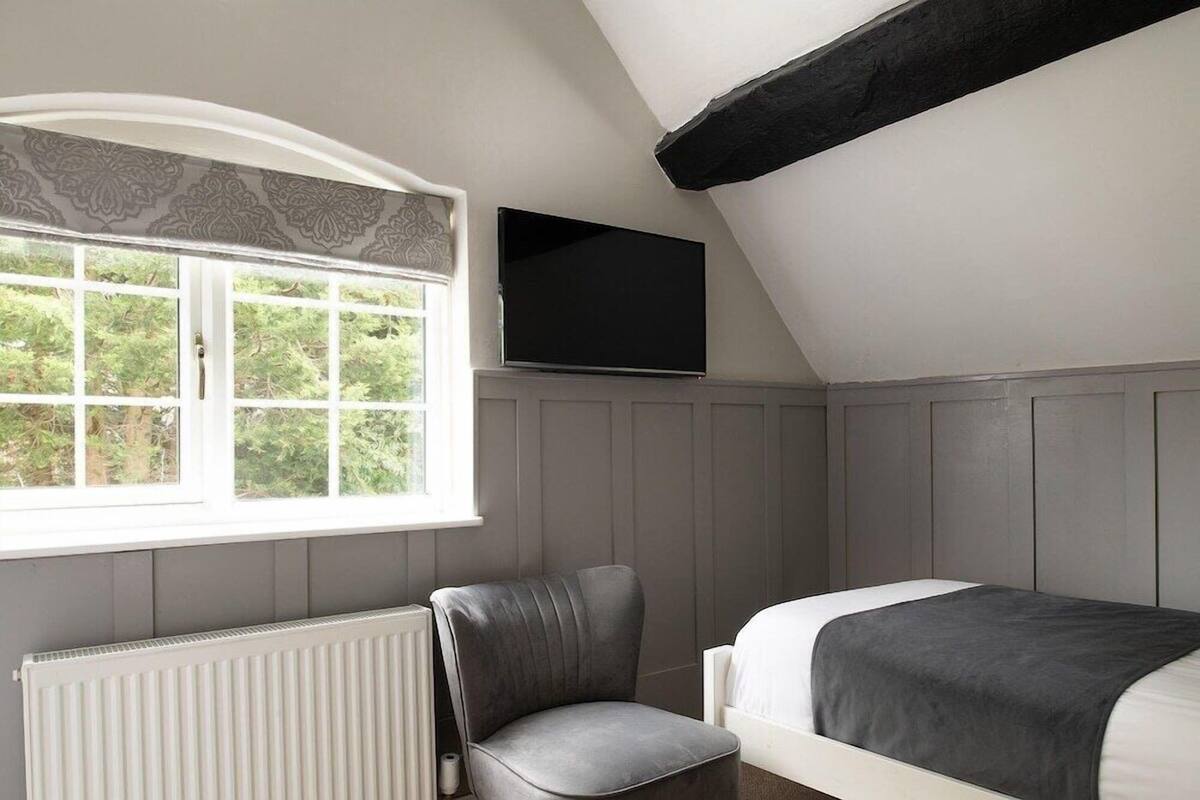A bedroom with a bed, a chair, a television, and a window with a view of greenery.