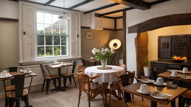 A dining area with a round table, chairs, and a vase of flowers. There is a window with a view of greenery outside.
