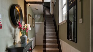 A staircase with a patterned carpet, a vase with flowers, and a mirror on the wall.