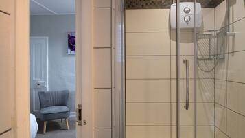 Un baño con cabina de ducha de vidrio, un perchero para toallas y un dispensador de jabón de pared.