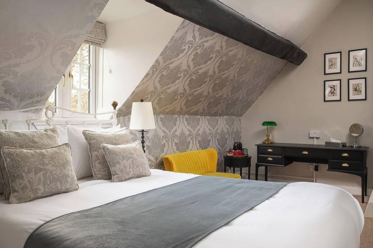 A bedroom with a bed, a nightstand, a desk, a chair, and a window.
