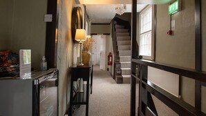 A hotel hallway with a staircase, a fire extinguisher, and a sign indicating the direction to the exit.