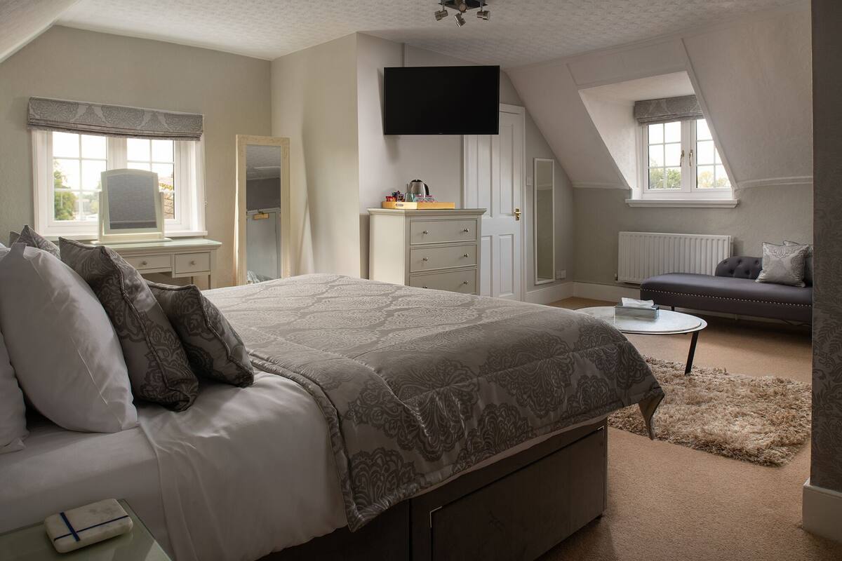 A bedroom with a large bed, a dresser, a TV, a desk, and a window.