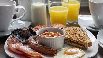 Een ontbijtbord met spek, worstjes, eieren, toast, bonen en tomaten.