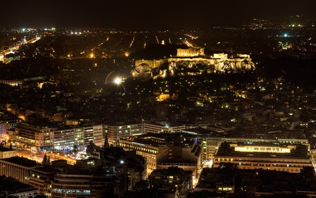 A cityscape at night with illuminated buildings and a prominent historical structure on a hill.