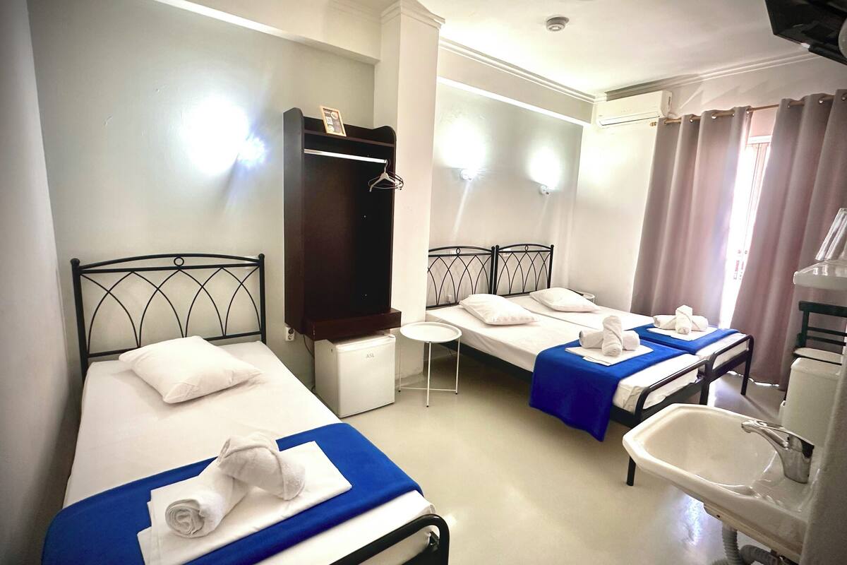 A hotel room with two single beds, a small round table, a mirror, a sink, and a wardrobe.