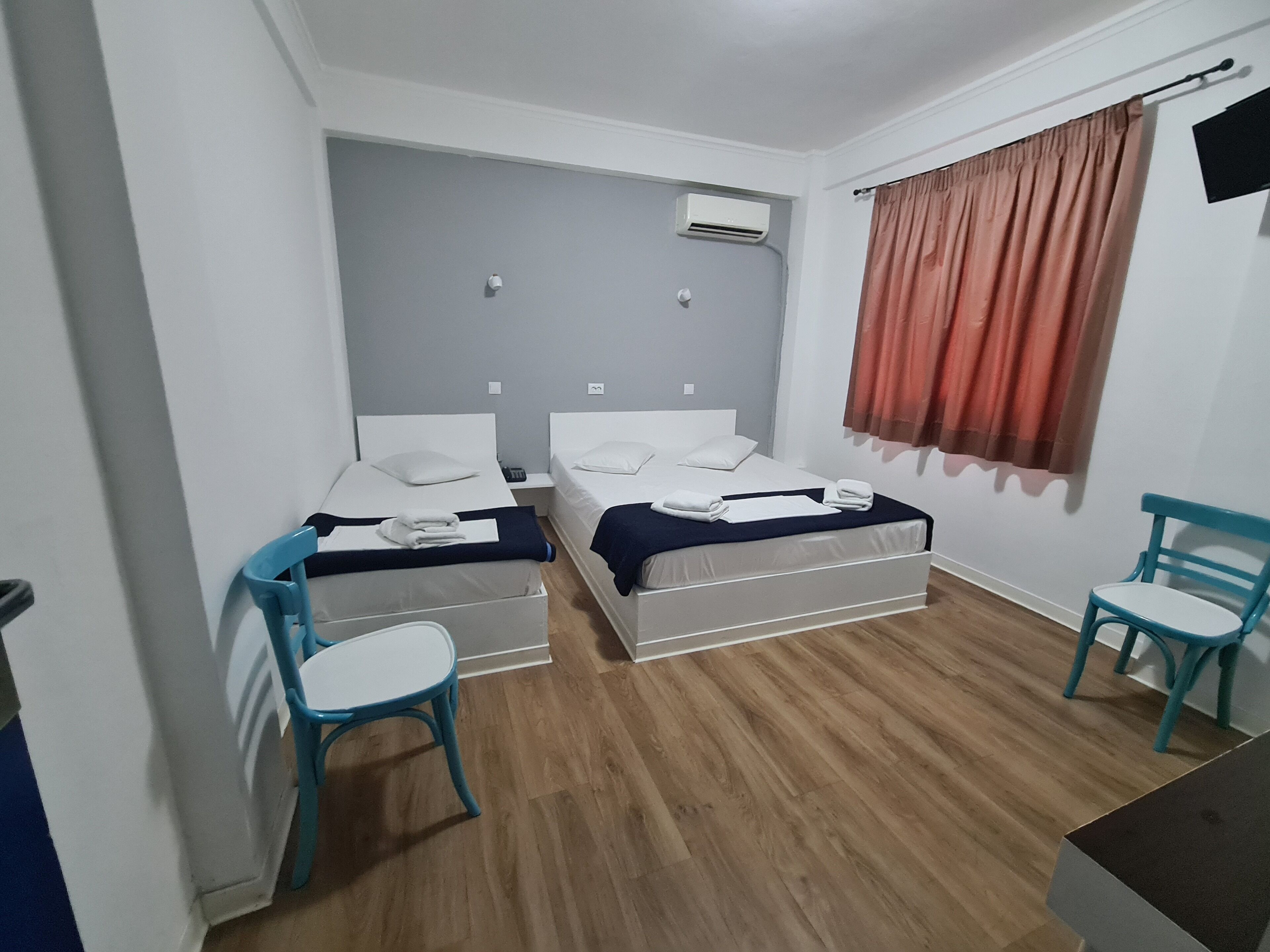 Et lille, rent værelse med to enkeltsenge, et skrivebord, to stole og en aircondition på væggen.