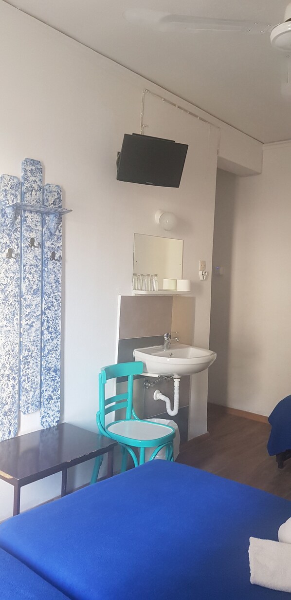 A room with a bed, a sink, a chair, and a television mounted on the wall.