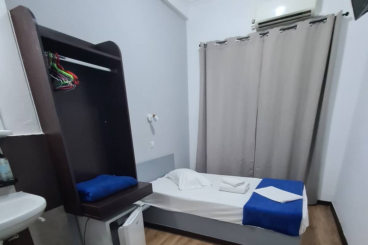 A compact hotel room with a bed, a small desk with a chair, a sink, and a wardrobe.