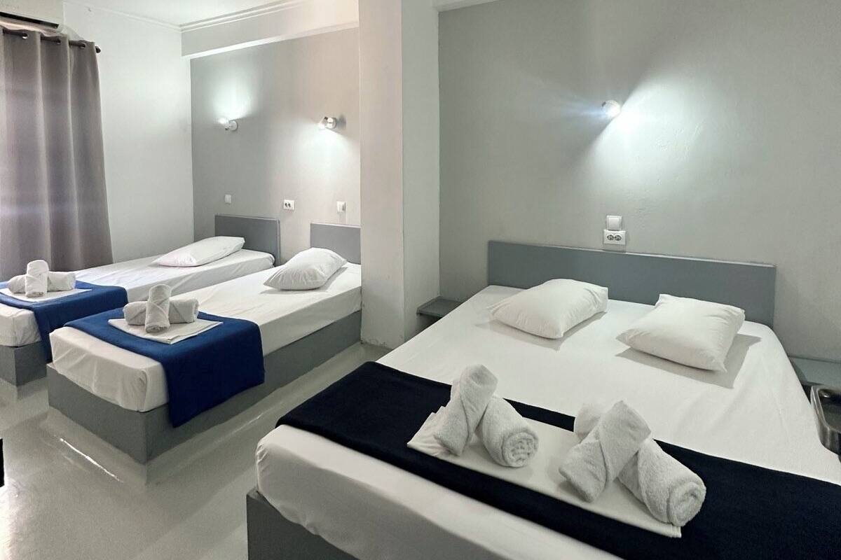 A modern hotel room with two single beds and a larger bed, all with white linens and towels.