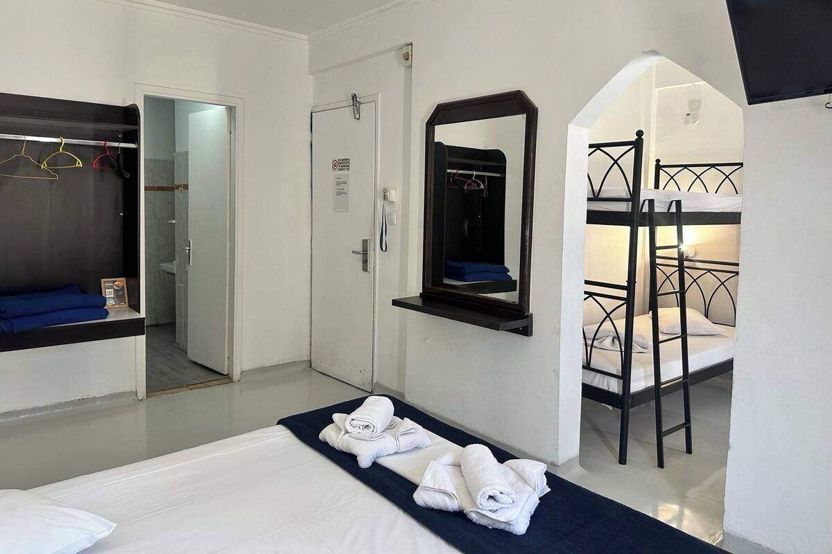 A hotel room with a bed, a wardrobe, a mirror, a bunk bed, and a door with a sign.